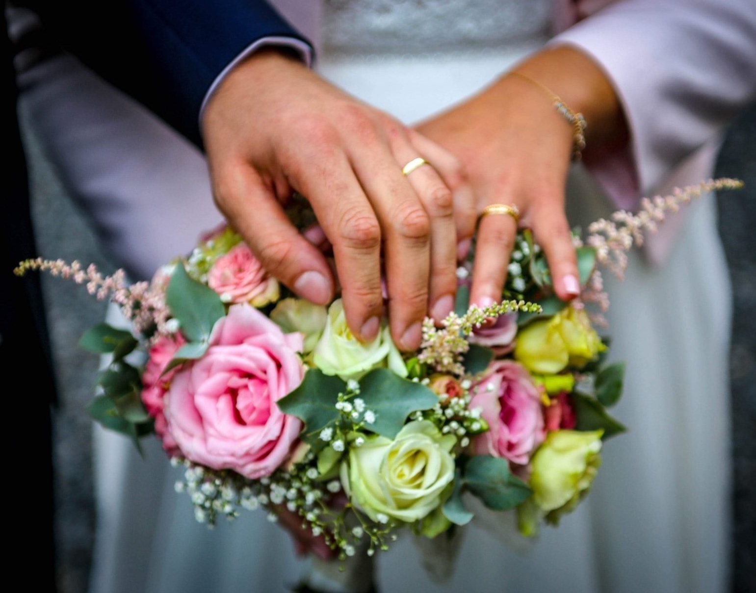 mains des mariés sur le bouquet de la mariée